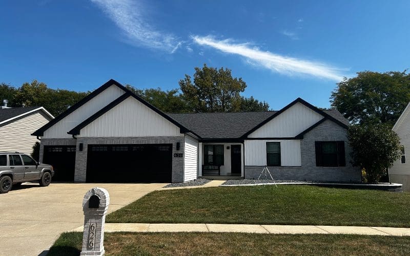 Modern single-story home in Greater St. Louis with black and white siding, three-car garage, and well-kept lawn under a clear sky.